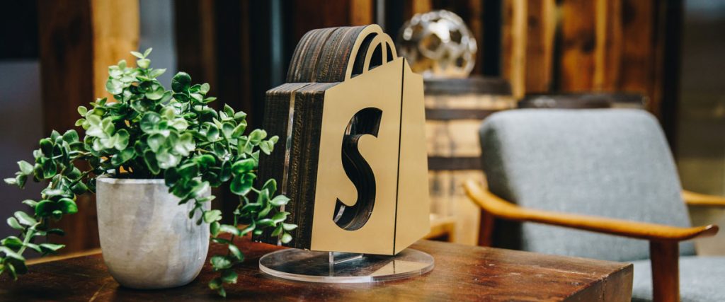 Wooden cutout Shopify logo on table with flower pot